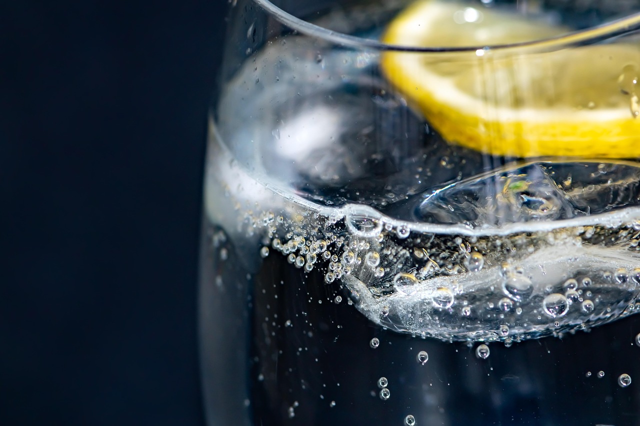 A tall glass of iced lemonade with lemon slices and bubbles